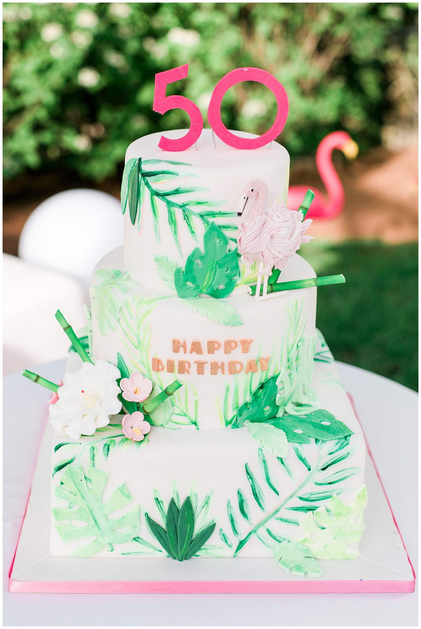 a 50th birthday cake with flamingos and greenery