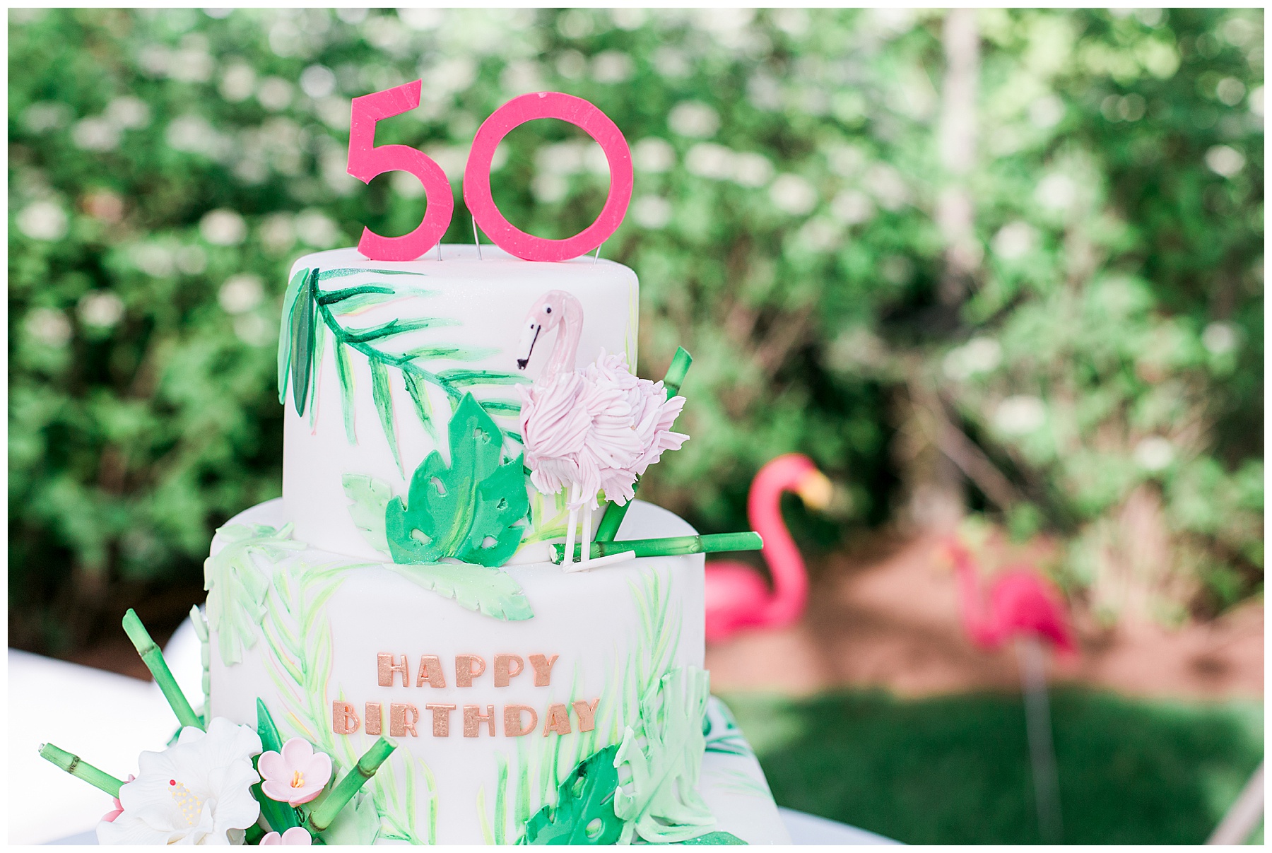a 50th birthday cake with flamingos and greenery