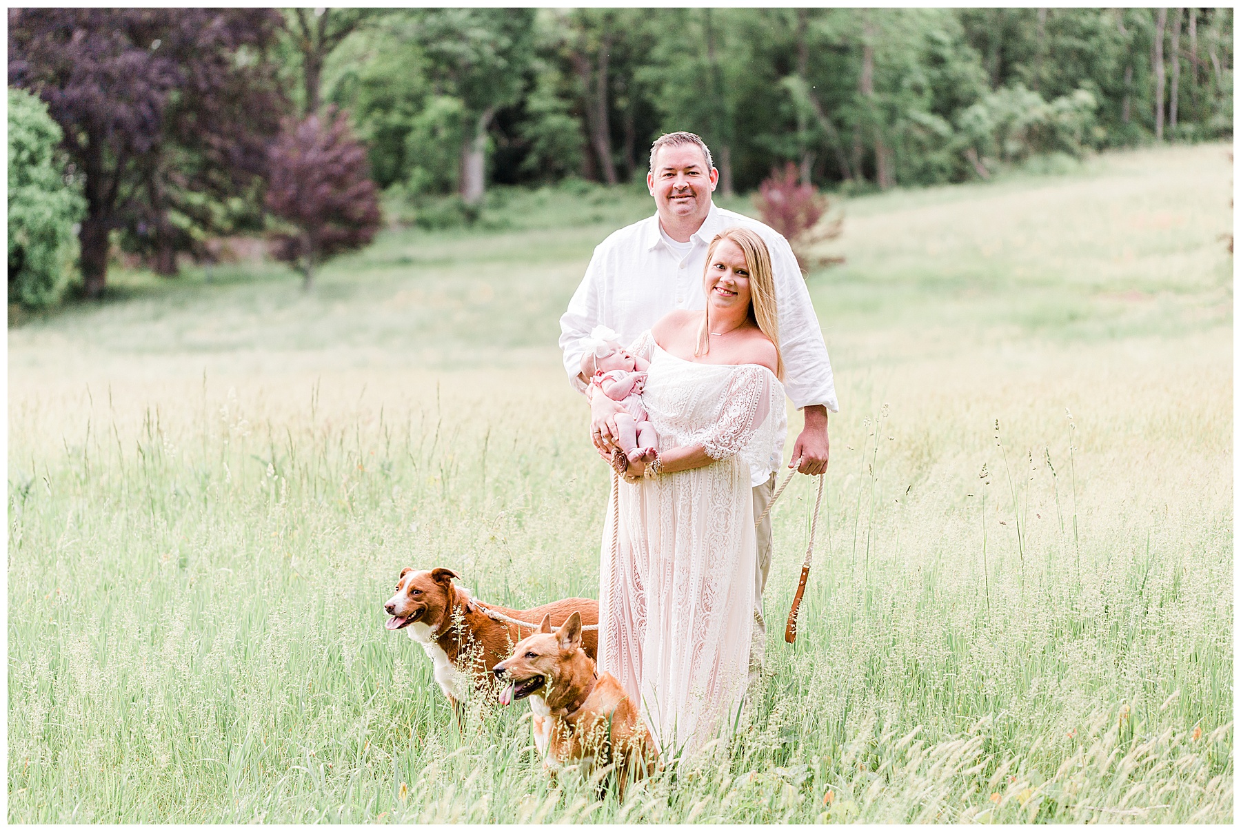Mom-and-dad-standing-in-field-with-dogs-and-baby